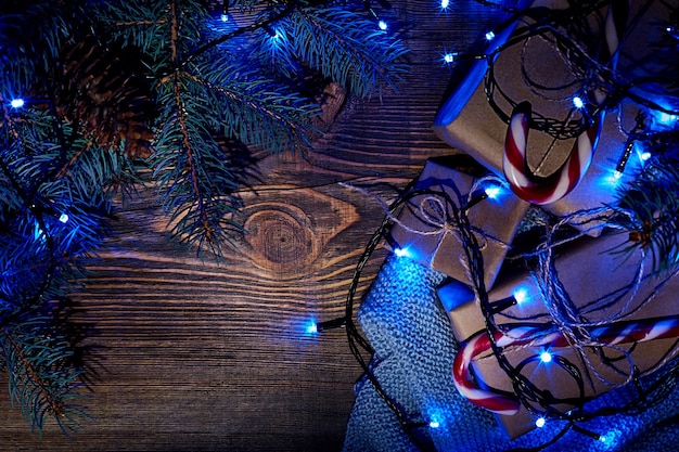Galho de árvore do abeto com luzes de Natal azuis, caixa de presente e bastões de doces em fundo de madeira com espaço de cópia. Vista do topo. Ainda vida.
