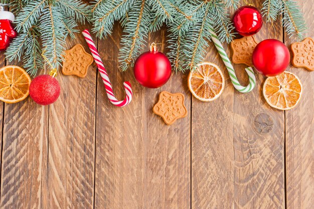 Galhos de árvore de Natal com enfeites, bastões de doces, laranjas secas e biscoitos em forma de estrela em fundo de madeira com espaço de cópia.