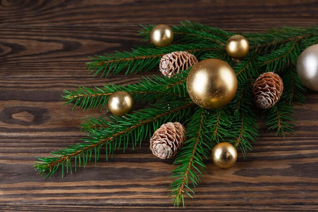 Galhos de pinheiro com bolas de Natal douradas e cones em um fundo de madeira marrom