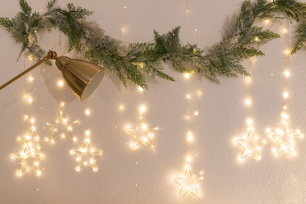 Galhos de uma árvore de Natal, uma guirlanda e uma lâmpada penduradas em uma parede branca Fundo de Natal Noite na véspera de Ano Novo Natal