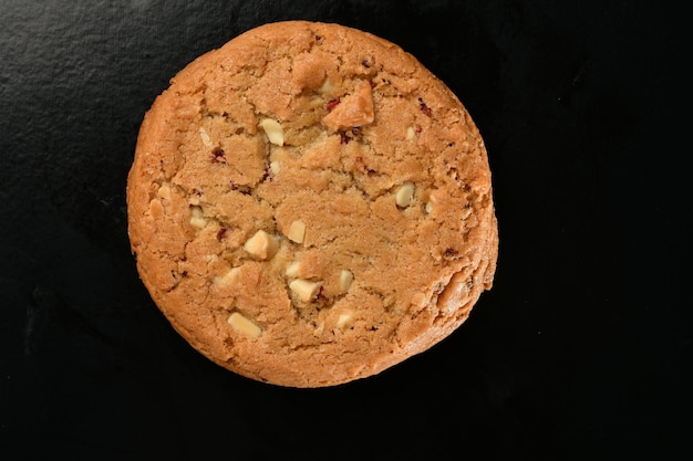 Una galleta con chocolate blanco y arándanos sobre un fondo negro