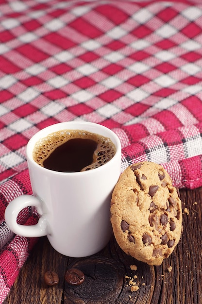 Galleta con chocolate y una taza de café caliente sobre el mantel encubierto de mesa de madera