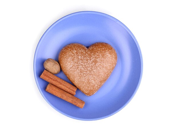 Galleta en forma de corazón con canela y nuez moscada en platillo aislado en blanco