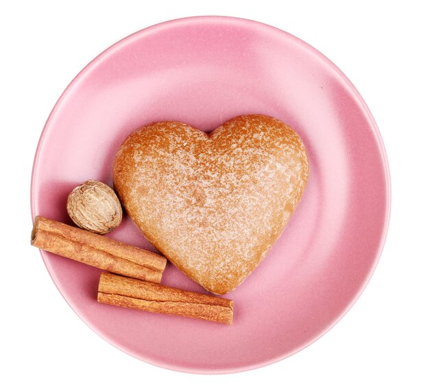 Galleta en forma de corazón con canela y nuez moscada en platillo aislado en blanco