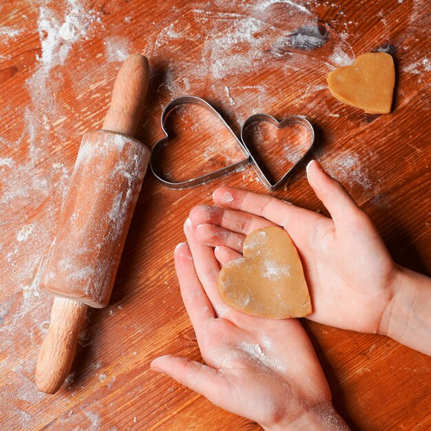 Galleta de galleta como corazón de masa en manos de niño Moldes de corazón rodillo y harina en una mesa Celebración del Día de San Valentín