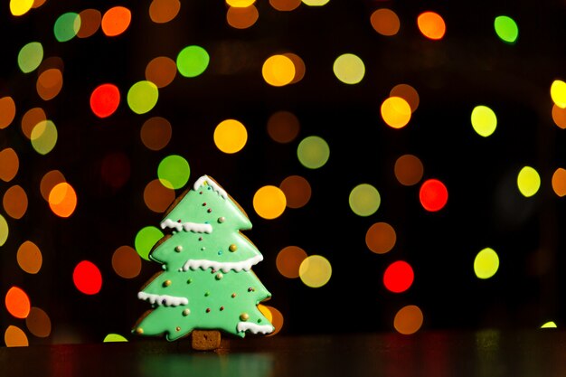 Galleta de jengibre de árbol de navidad verde sobre luces de guirnaldas de colores desenfocadas