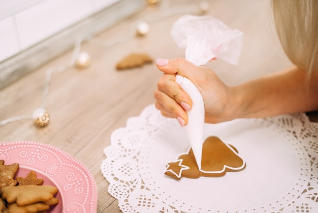 Galleta de jengibre. La mano de la mujer dibuja con esmalte un árbol de Navidad en una servilleta blanca. Preparativos navideños.