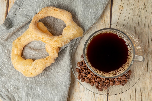 Galleta de mandioca de café caliente conocida como biscoito de polvilho en portugués y granos de café en una mesa de madera con vista superior del área de texto de taza completa