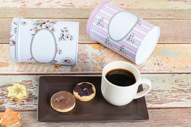 Galleta mantecosa con una flor seca encima, junto a otras galletas, taza de café y latas acostadas.