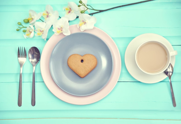 Galleta de pan de jengibre en forma de corazón en un plato gris con una taza de café vista superior Mesa de madera antigua