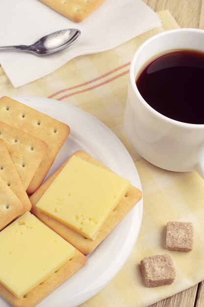 Galleta con queso y una taza de café negro sobre la mesa de madera antigua