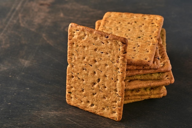 Galleta con semillas de lino y forma rectangular de salvado de avena para una dieta sana, dietética y equilibrada sobre fondo de madera oscura. Merienda para una nutrición adecuada.