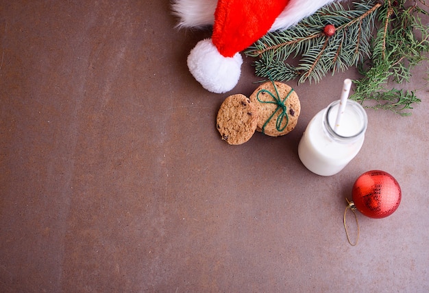 Galletas de año nuevo para santa con leche, en platos blancos y con chocolate. Sombrero de Santa, juguetes en el árbol de Navidad, ramitas de árbol de Navidad. Endecha plana