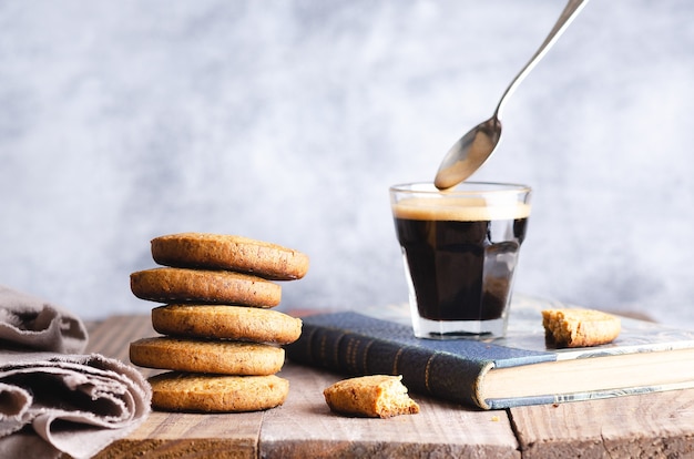 Galletas apiladas y una taza de café en un libro azul y una servilleta beige sobre una mesa de madera