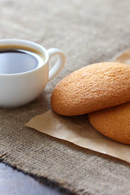 Galletas de avena atadas y una taza de café sobre papel kraft y mantel de arpillera. Marco vertical