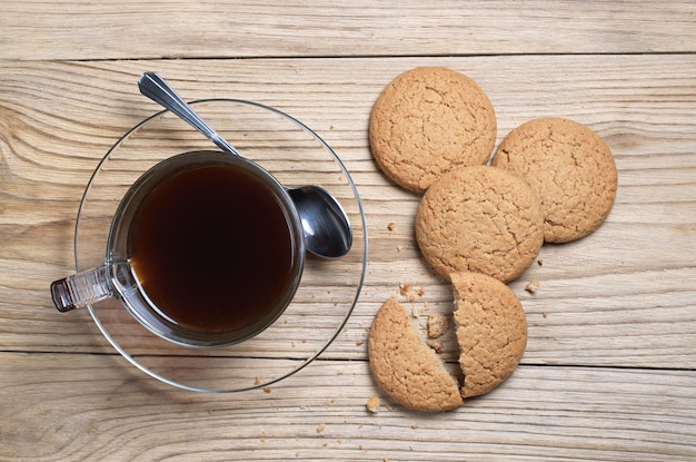 Galletas de avena y café negro en una taza transparente para el desayuno en la vista superior de fondo de madera vieja