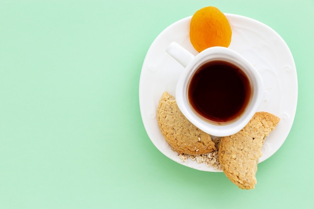 Galletas de avena caseras sin gluten, albaricoque seco y taza de té o café expreso en verde pastel