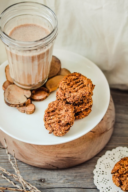 Galletas de avena y mantequilla de maní con un vaso de leche de cáñamo no lácteos sobre madera