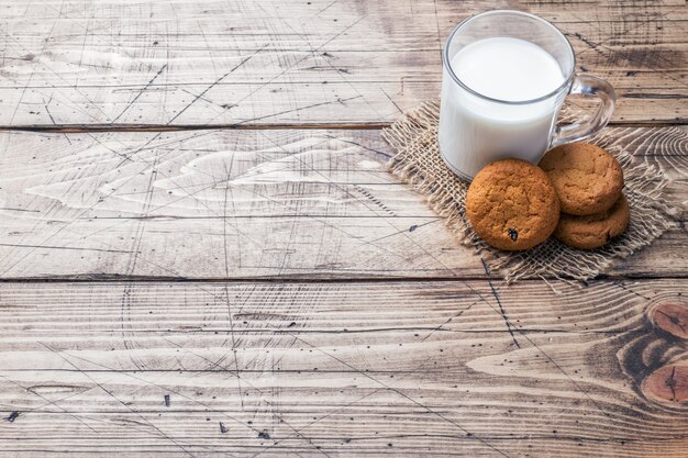 Galletas de avena naturales y un vaso de leche sobre un fondo de madera