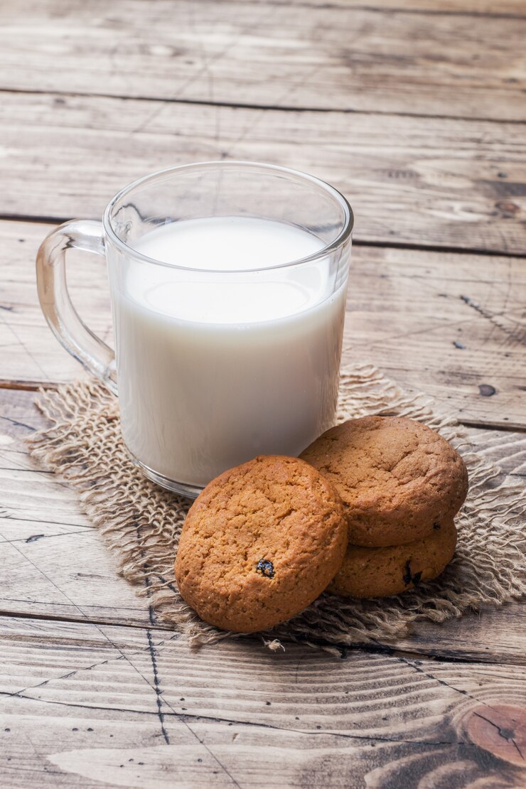Galletas de avena naturales y un vaso de leche sobre un fondo de madera
