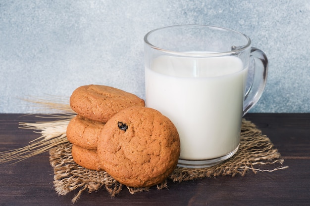 Galletas de avena naturales y un vaso de leche sobre un fondo de madera