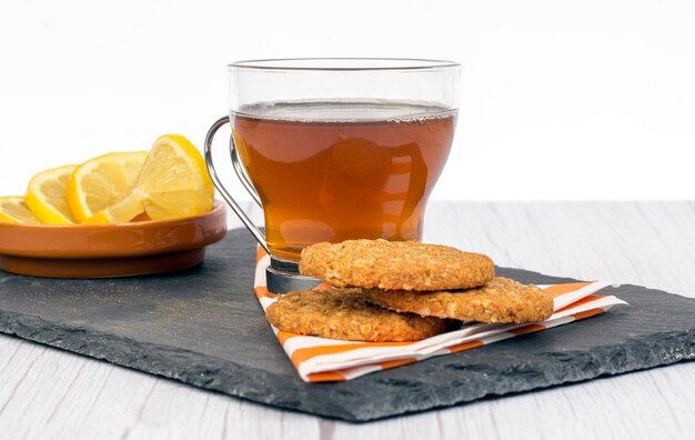 Galletas de avena y té con limón en una bandeja sobre una superficie blanca.