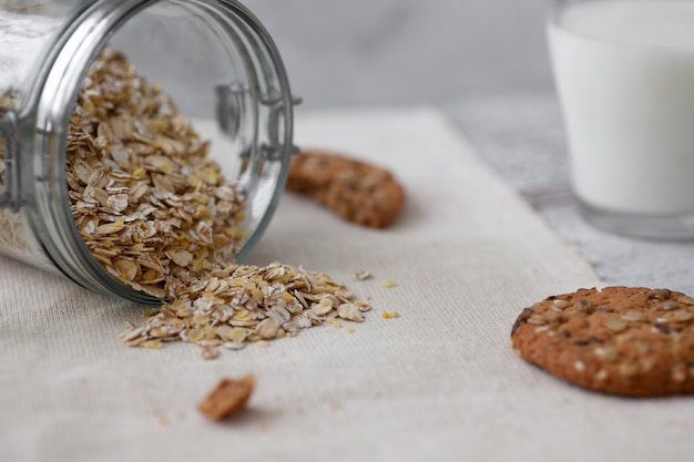 Galletas de avena, un vaso de leche, cereales en una mesa de madera y un gris