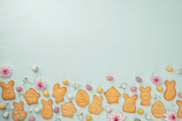 Galletas de azúcar en forma de conejito con huevos de chocolate de Pascua y fondo de flores Felices Pascuas