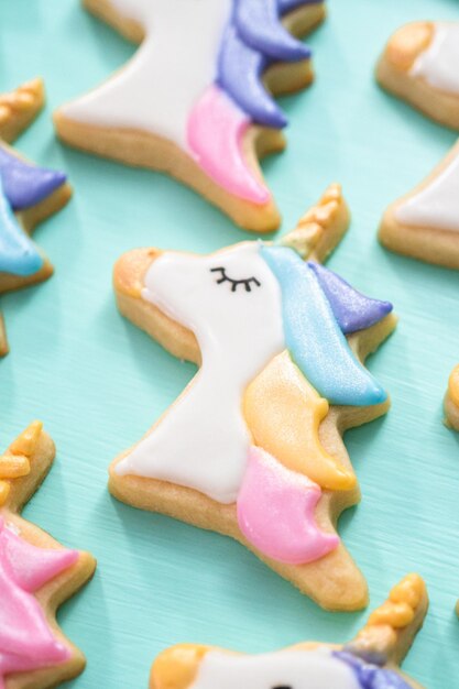 Galletas de azúcar de unicornio decoradas con glaseado real y purpurina de comida sobre un fondo azul.