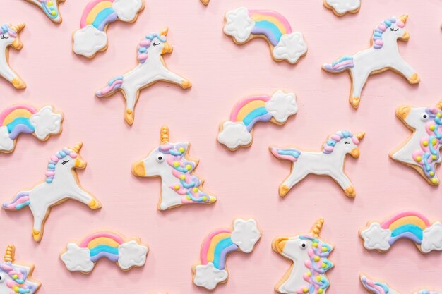 Galletas de azúcar de unicornio decoradas con glaseado real sobre fondo rosa.