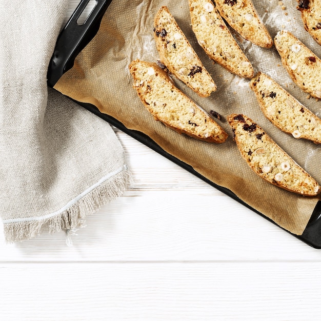 Galletas biscotti italianas en una bandeja para hornear negra y una mesa blanca.