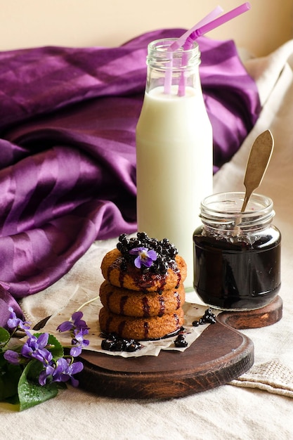 Galletas con botella de mermelada de leche y flores de violetas en la mesa