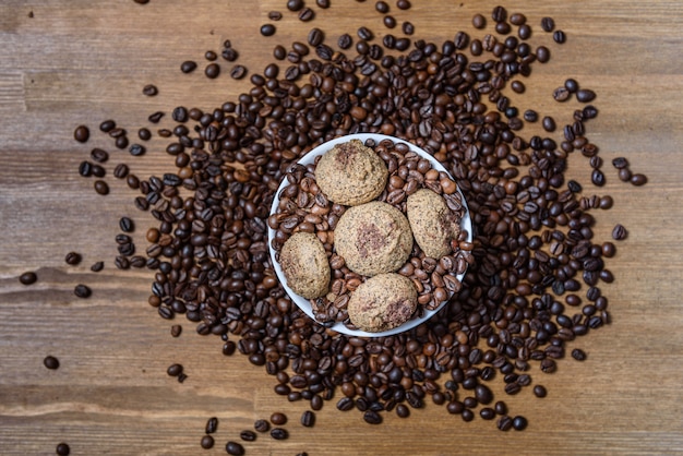 Galletas de café en un plato blanco con granos de café en la mesa de madera marrón