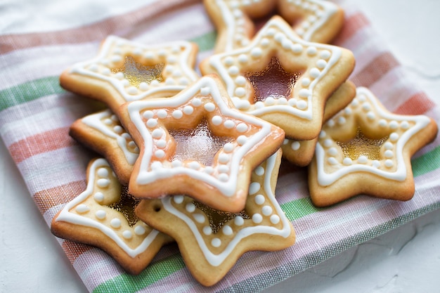 Galletas caseras de caramelo de azúcar con forma de estrella de Navidad en una servilleta de rayas de colores sobre fondo blanco.