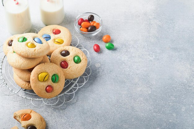 Galletas caseras con coloridos dulces de chocolate y leche Pila de galletas de mantequilla con dulces multicolores en un plato con una botella de leche sobre fondo gris claro Concepto de comida para bebés Espacio de copia