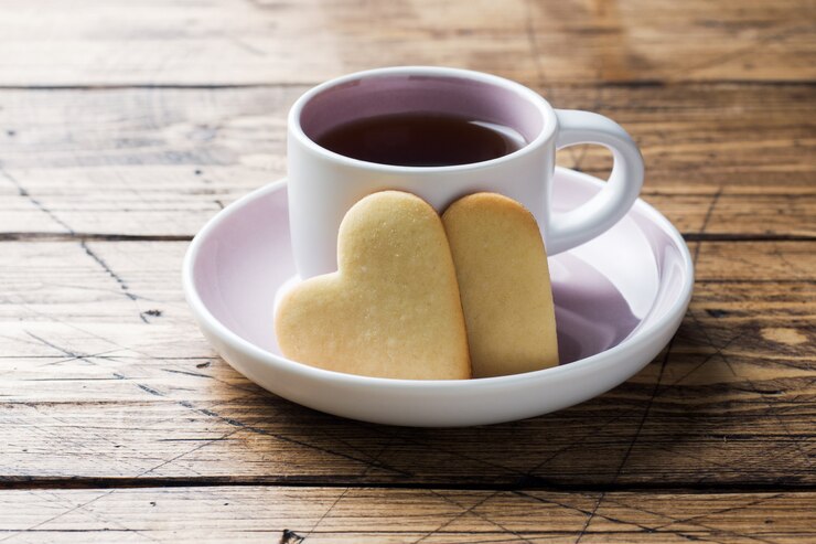 Galletas caseras del corazón y taza de café en una placa