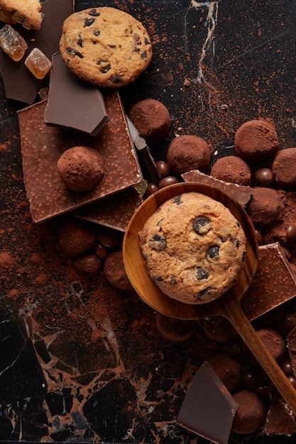 Galletas caseras en una cuchara de madera con chocolate y cacao en polvo sobre un fondo oscuro