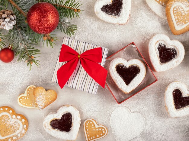 Galletas caseras en forma de corazón con mermelada de frambuesa en mesa de madera blanca para Navidad o San Valentín. Vista superior.