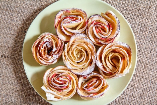 Galletas caseras con manzanas en forma de rosa sobre fondo de placa y tela de saco Vista superior