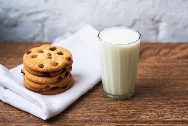 Galletas caseras sabrosas fragantes con pasas y un vaso de leche fresca en la toalla de cocina blanca