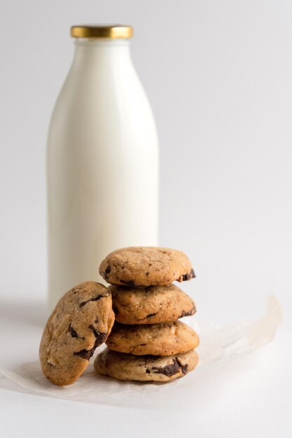 Galletas caseras con trozos de chocolate en el fondo de una botella de leche en un fondo blanco