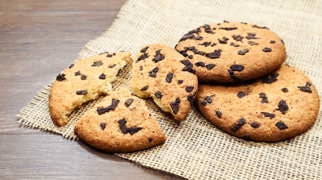 Galletas de chispas de chocolate americano en una mesa de madera marrón y en un primer plano de una servilleta de lino. Masa tradicional redondeada y crujiente con chispas de chocolate. Panadería. Postre delicioso, repostería. Bodegón rural.