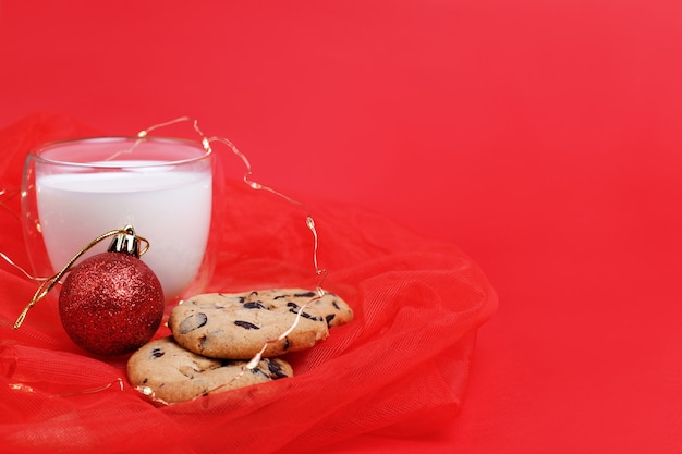 Galletas con chispas de chocolate, un vaso de leche y un árbol de Navidad de juguete rojo sobre un fondo de Año Nuevo