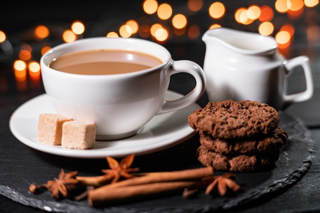 Galletas de chocolate, café, especias en luces de Navidad borrosas.