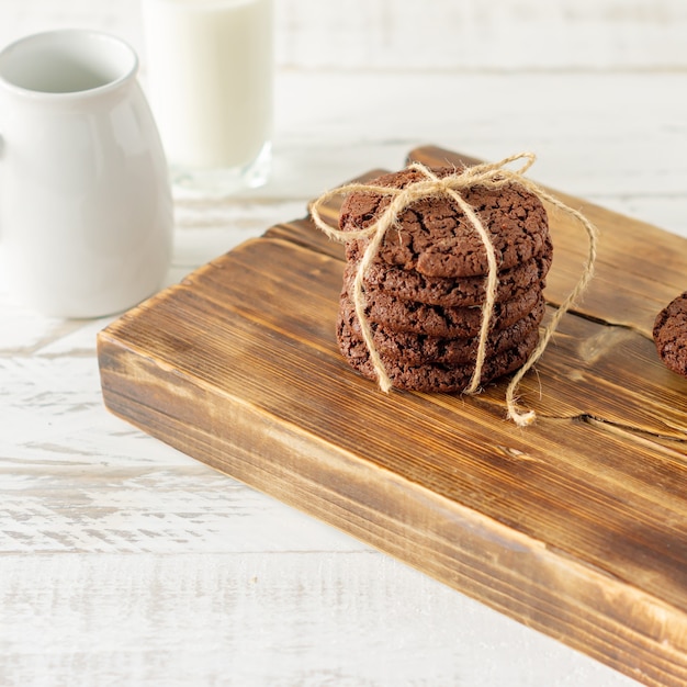 Galletas de chocolate para el desayuno con un vaso de leche en una mesa de madera blanca.