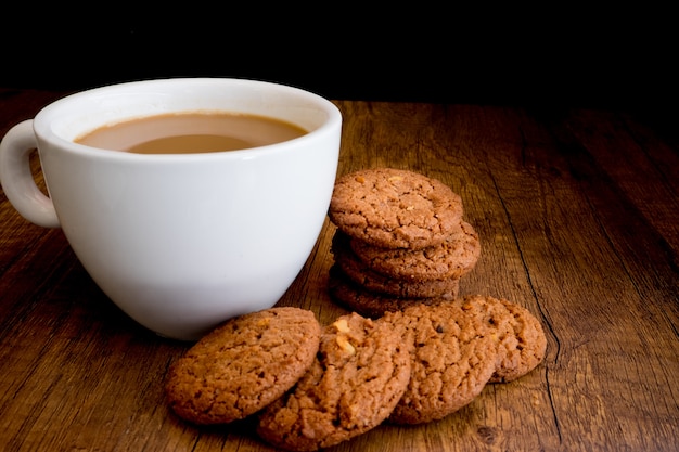 Las galletas de chocolate hechas en casa comen con café caliente en fondo de madera