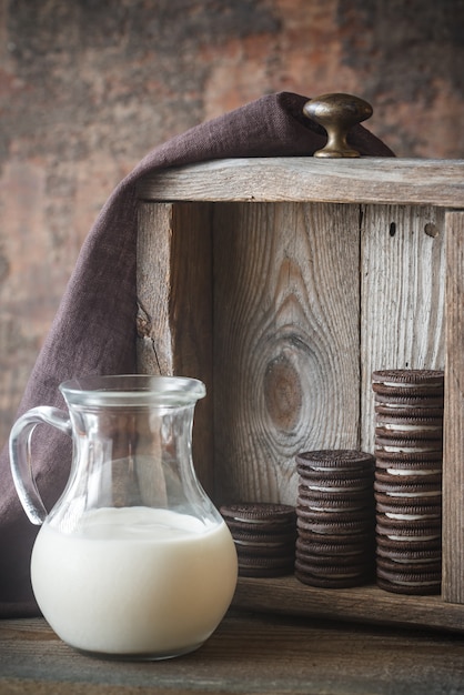 Foto galletas de chocolate con relleno cremoso con jarra de leche
