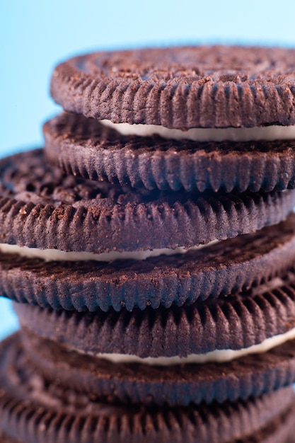 Foto galletas de chocolate sándwich negro marrón macro con crema de leche blanca sobre fondo azul delicioso sabroso