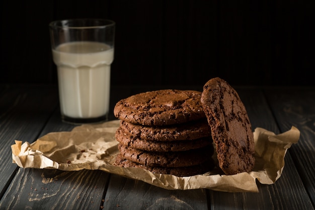 Galletas de chocolate sobre papel artesanal con vaso de leche.