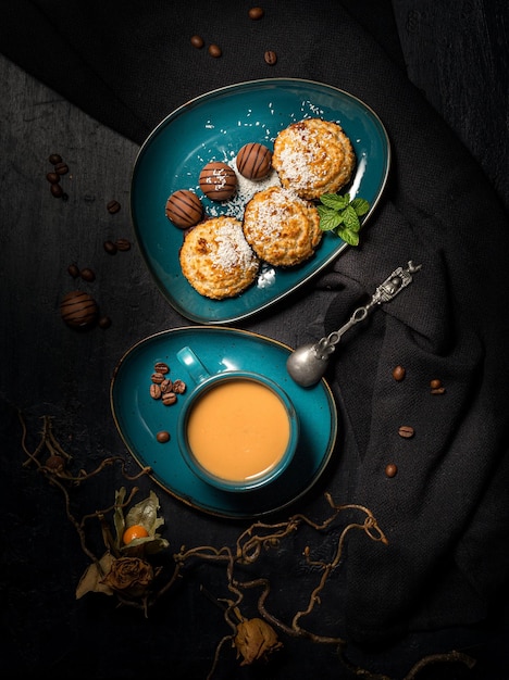 galletas de coco con chocolate en un plato verde azulado oscuro, una taza de café con leche en un respaldo negro